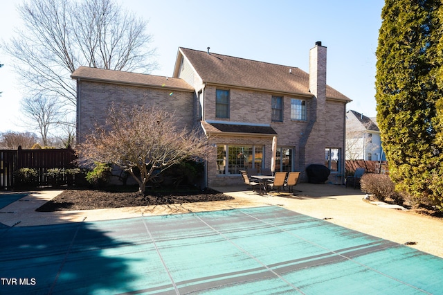 back of property featuring brick siding, a chimney, fence, and a patio