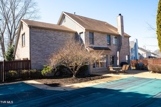 rear view of house featuring a fenced in pool, a patio, a chimney, fence, and brick siding