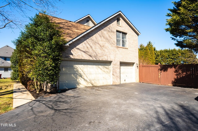 view of side of home with brick siding, fence, driveway, and an attached garage