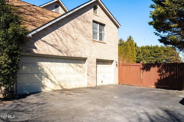 view of home's exterior with aphalt driveway, an attached garage, fence, and brick siding