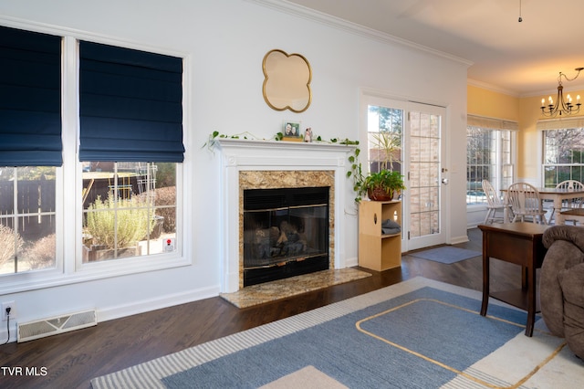 living room featuring a premium fireplace, wood finished floors, visible vents, ornamental molding, and an inviting chandelier