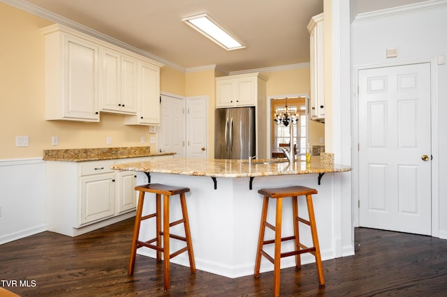 kitchen with dark wood finished floors, ornamental molding, light stone counters, freestanding refrigerator, and a peninsula