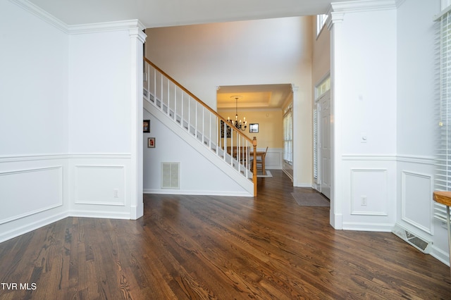 foyer entrance with a notable chandelier, visible vents, stairs, dark wood-style floors, and ornate columns