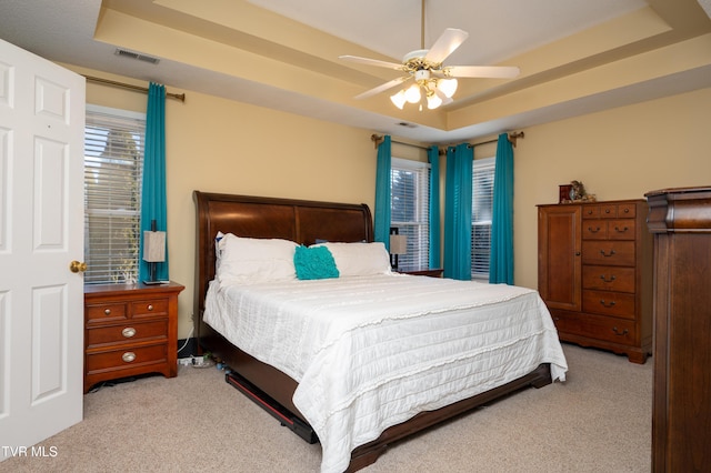 bedroom with carpet floors, a tray ceiling, visible vents, and a ceiling fan