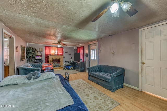 bedroom featuring ceiling fan, a textured ceiling, a fireplace with raised hearth, and wood finished floors