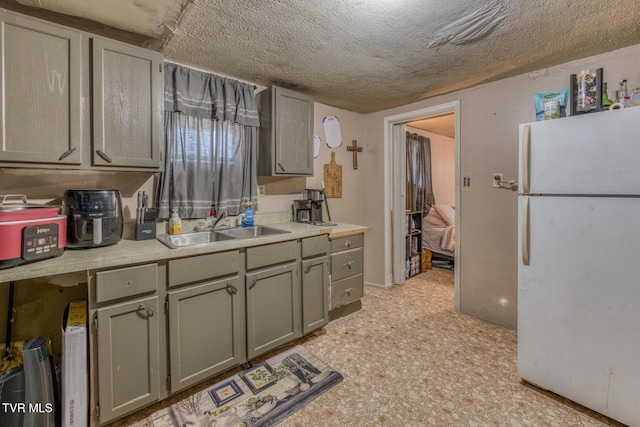 kitchen with a textured ceiling, gray cabinetry, a sink, light countertops, and freestanding refrigerator