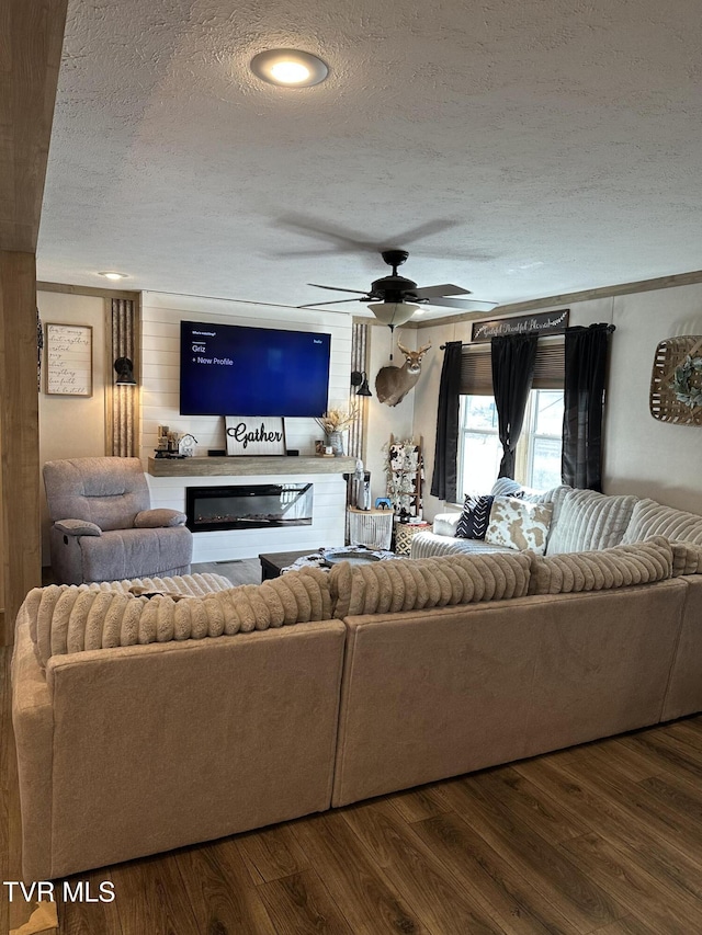 living room featuring a glass covered fireplace, dark wood-style flooring, ceiling fan, and a textured ceiling