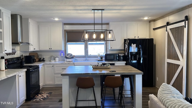 kitchen with wall chimney exhaust hood, white cabinets, black appliances, and a barn door