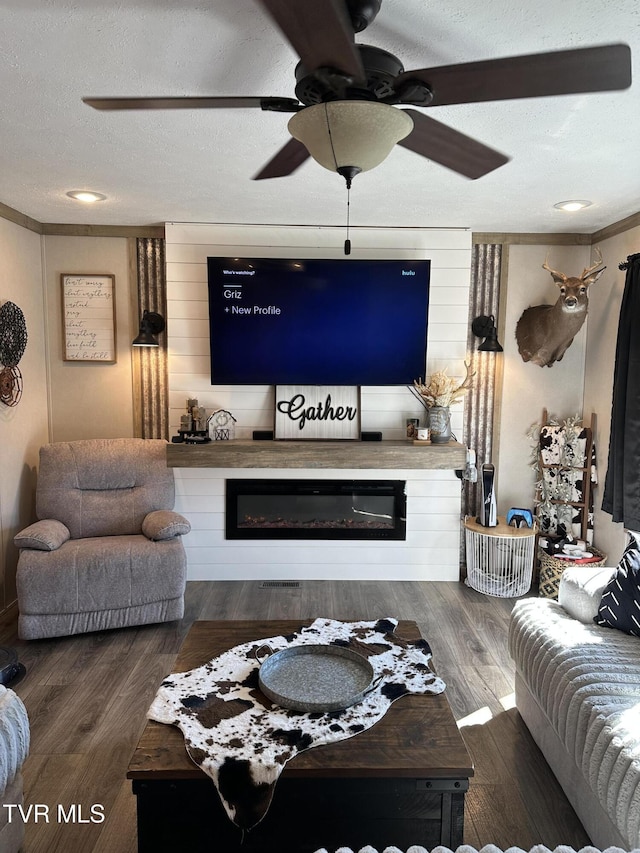 living area with a textured ceiling, a glass covered fireplace, wood finished floors, and ornamental molding