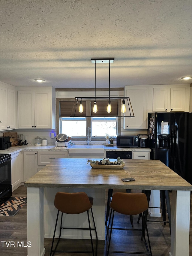 kitchen featuring butcher block countertops, a breakfast bar, black appliances, white cabinetry, and a sink