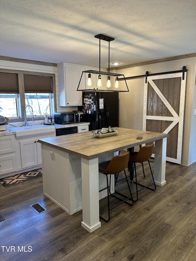 kitchen featuring a barn door, dark wood-style flooring, wood counters, white cabinets, and black appliances