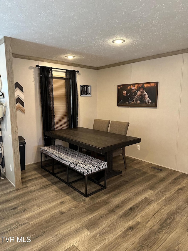 dining space with a textured ceiling, ornamental molding, and wood finished floors