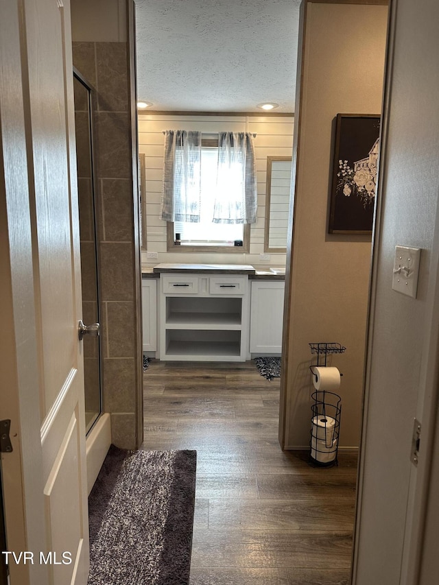 full bath featuring a shower with door, a textured ceiling, wood finished floors, and vanity