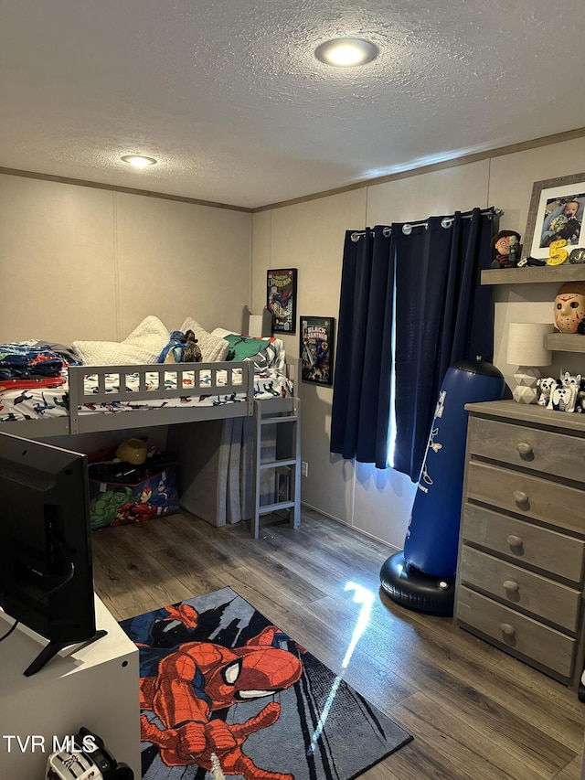 bedroom with a textured ceiling, wood finished floors, and crown molding