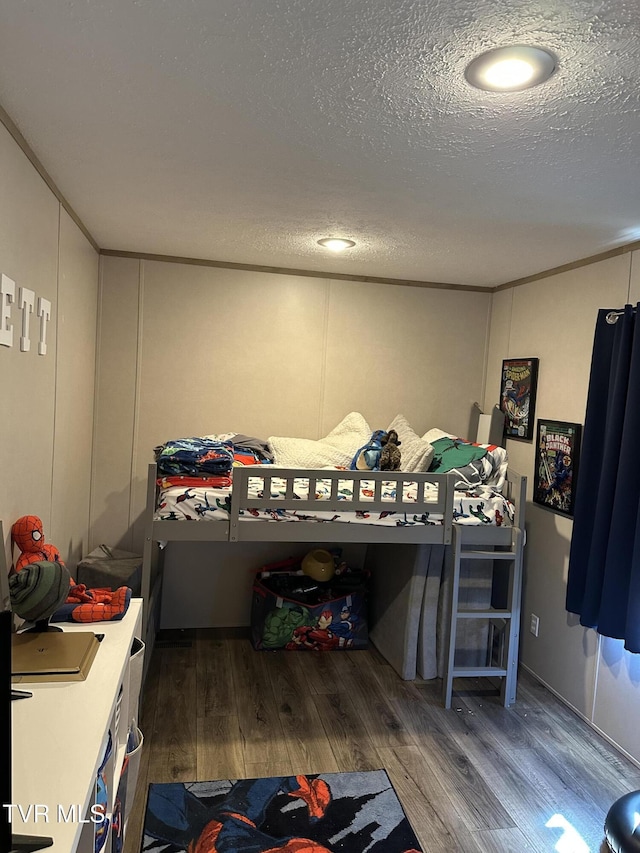 bedroom with crown molding, a textured ceiling, and wood finished floors