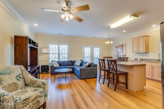 living room with ornamental molding, light wood finished floors, ceiling fan with notable chandelier, and recessed lighting