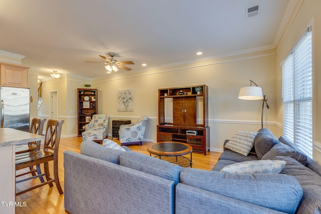 living room with ceiling fan, ornamental molding, visible vents, and light wood-style flooring