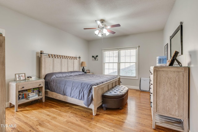 bedroom featuring light wood-type flooring, a textured ceiling, a barn door, baseboards, and ceiling fan