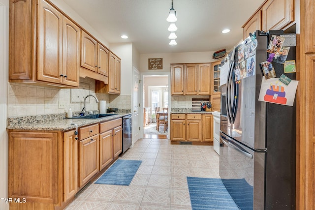 kitchen featuring light floors, light stone counters, dishwashing machine, freestanding refrigerator, and a sink