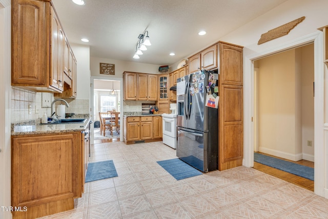 kitchen featuring stainless steel refrigerator with ice dispenser, a sink, light stone counters, tasteful backsplash, and white electric range oven