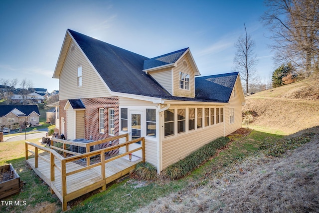 back of house featuring brick siding, a shingled roof, a deck, and a sunroom