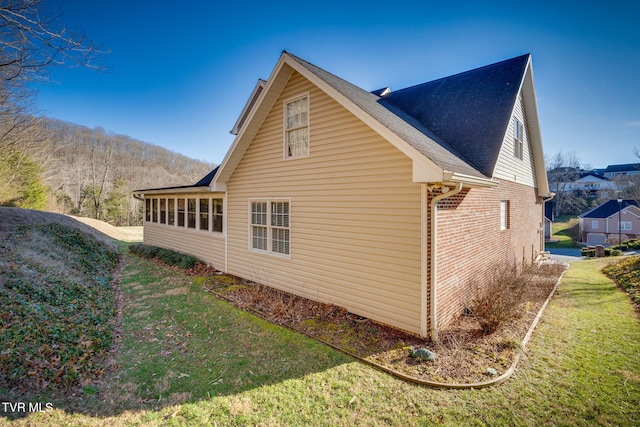 view of home's exterior featuring a sunroom, a yard, brick siding, and roof with shingles