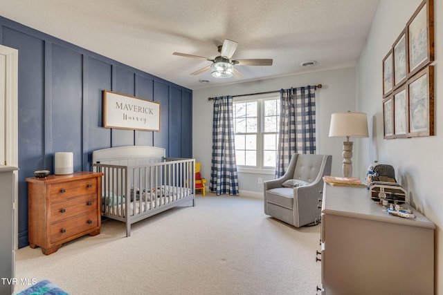 bedroom featuring visible vents, carpet floors, ceiling fan, a crib, and a textured ceiling