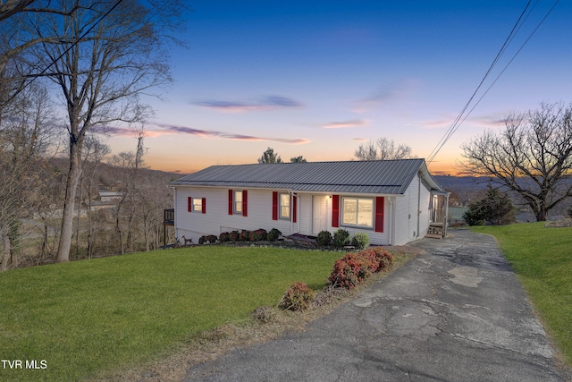 view of front of property featuring aphalt driveway, metal roof, and a lawn