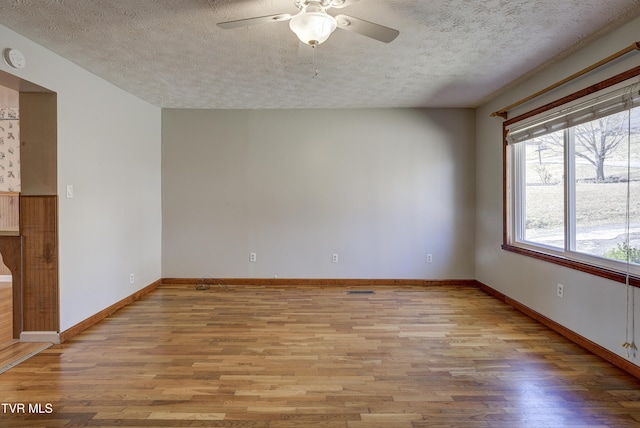 empty room featuring a ceiling fan, light wood-type flooring, a textured ceiling, and baseboards