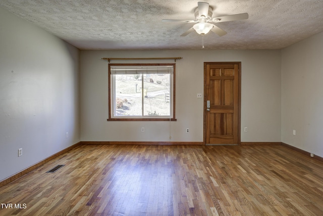 unfurnished room with a textured ceiling, wood finished floors, visible vents, and baseboards