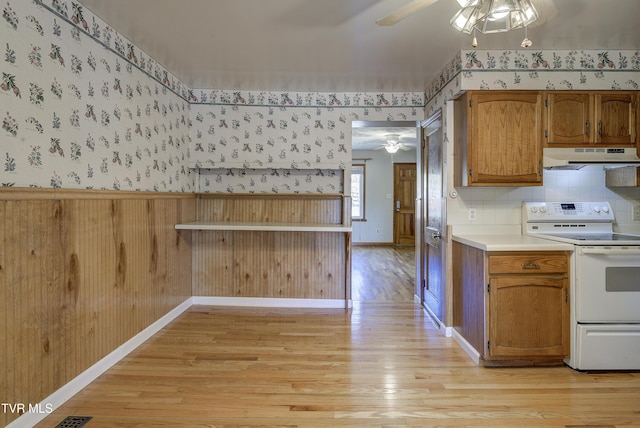 kitchen with a wainscoted wall, white electric range, a ceiling fan, under cabinet range hood, and wallpapered walls