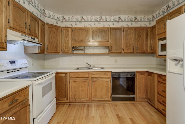 kitchen featuring under cabinet range hood, white appliances, a sink, light wood finished floors, and brown cabinetry