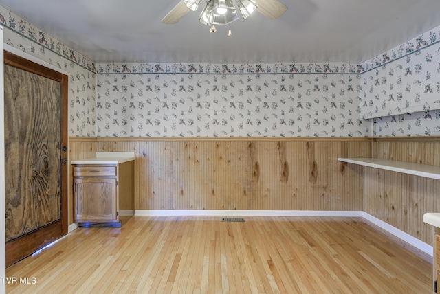 interior space with a wainscoted wall, a ceiling fan, light wood-style flooring, and wallpapered walls