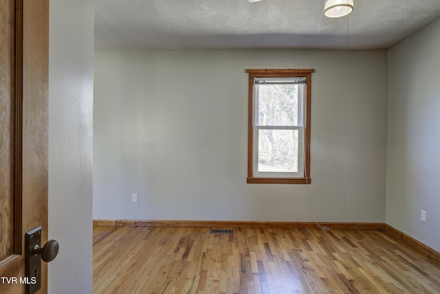 unfurnished room with a textured ceiling, wood finished floors, visible vents, and baseboards