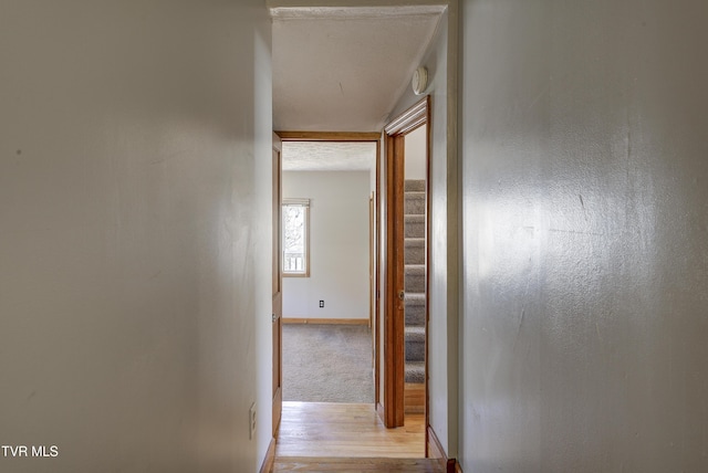 corridor featuring light wood-style floors, baseboards, and stairs