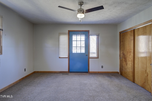 interior space featuring a textured ceiling, carpet floors, a ceiling fan, visible vents, and baseboards