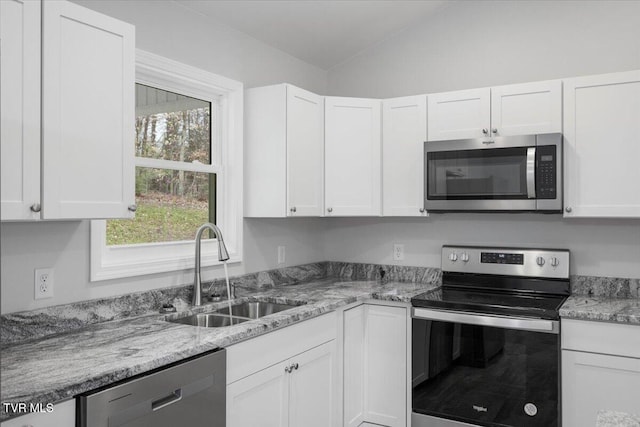 kitchen featuring light stone counters, stainless steel appliances, lofted ceiling, white cabinetry, and a sink