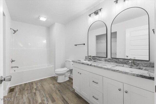 full bath with toilet, tub / shower combination, a sink, and wood finished floors