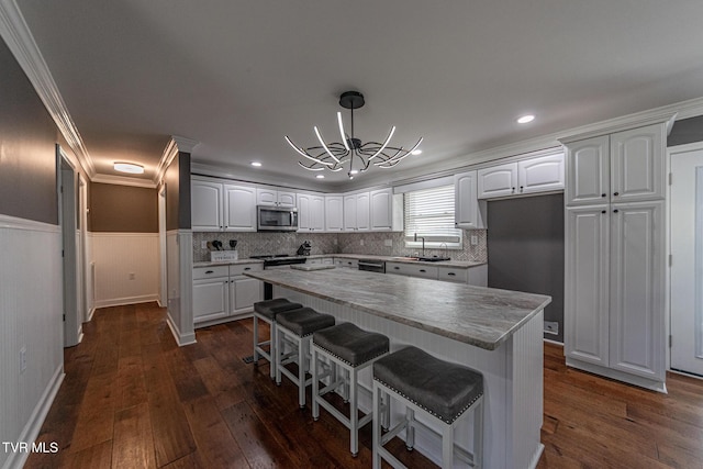 kitchen featuring a wainscoted wall, white cabinetry, stainless steel microwave, and dark wood-type flooring