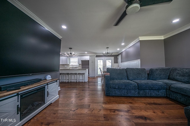 living area with dark wood-style floors, recessed lighting, ornamental molding, and ceiling fan with notable chandelier