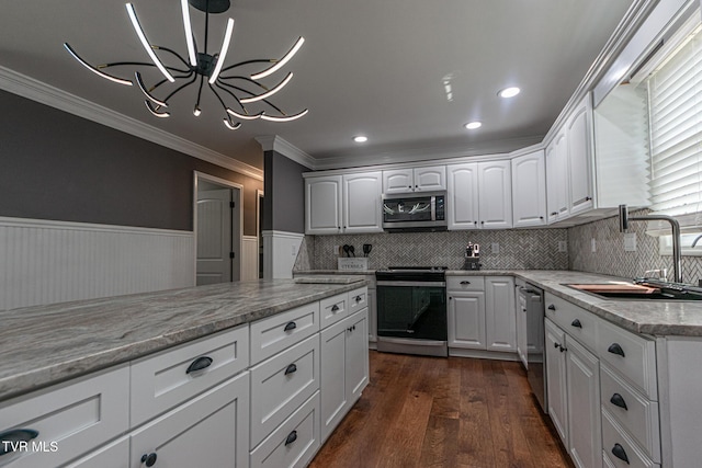 kitchen with a wainscoted wall, stainless steel appliances, dark wood-type flooring, a sink, and ornamental molding