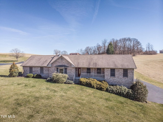 ranch-style house featuring a front yard, brick siding, covered porch, and roof with shingles