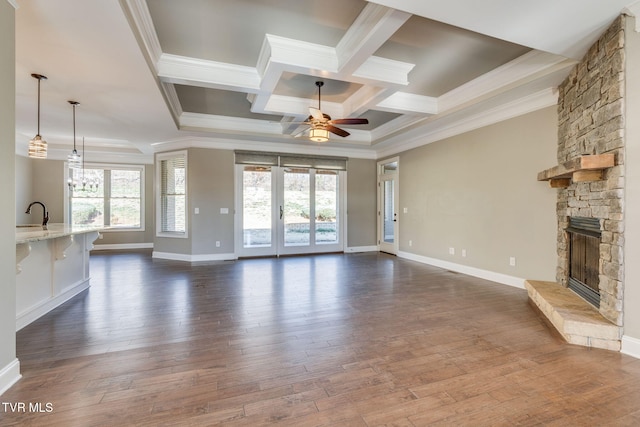 unfurnished living room with ceiling fan with notable chandelier, ornamental molding, dark wood-style flooring, and a stone fireplace