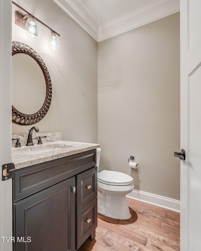 bathroom featuring toilet, wood finished floors, vanity, baseboards, and crown molding