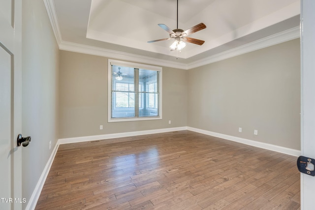 spare room with a tray ceiling, wood finished floors, and baseboards