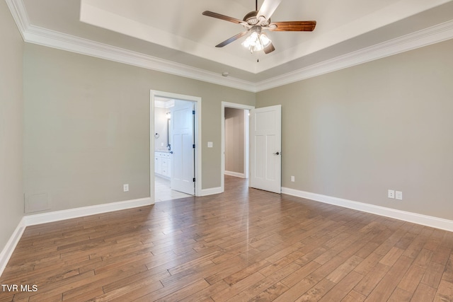 empty room featuring ceiling fan, wood finished floors, baseboards, ornamental molding, and a tray ceiling