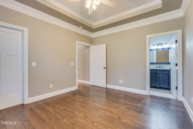 unfurnished bedroom with a tray ceiling, a sink, dark wood finished floors, and baseboards