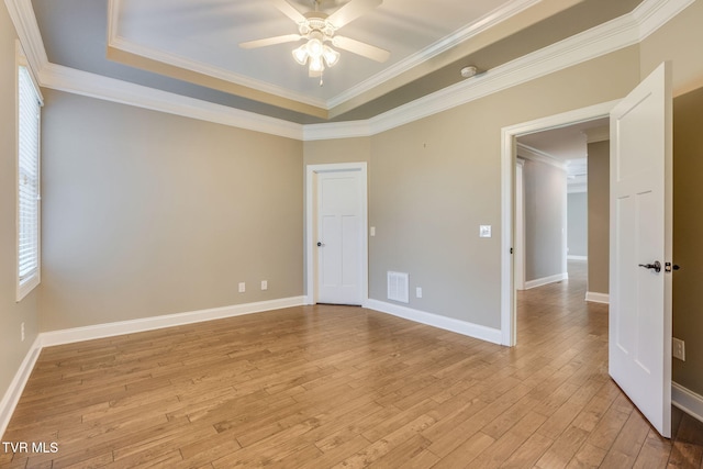 spare room featuring light wood-style floors, baseboards, visible vents, and a tray ceiling