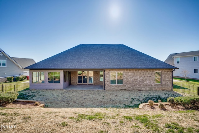 rear view of property with brick siding, fence, a patio, and roof with shingles