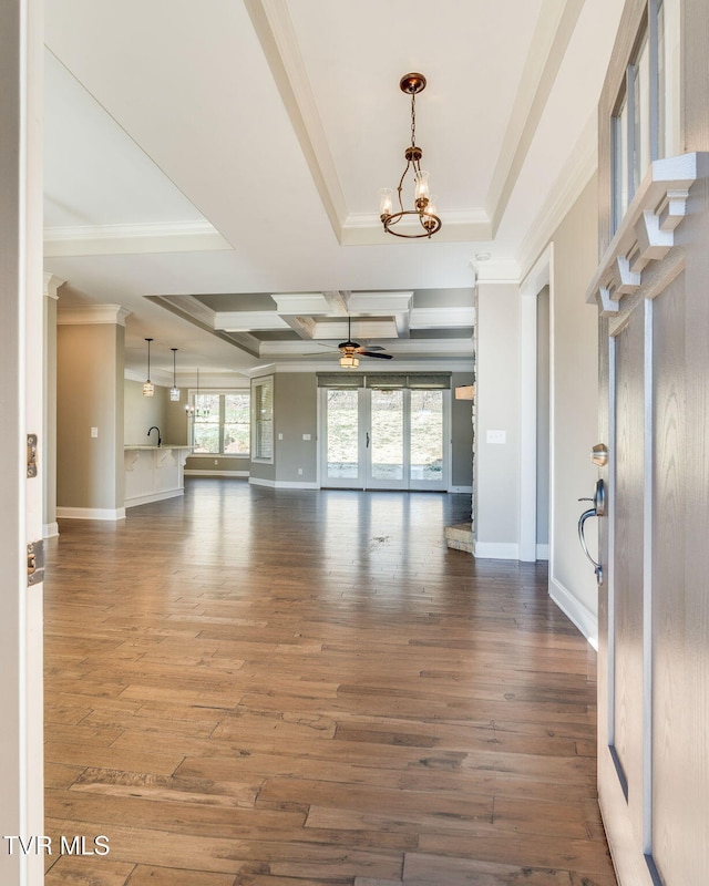 unfurnished living room featuring ceiling fan with notable chandelier, a tray ceiling, wood finished floors, and crown molding